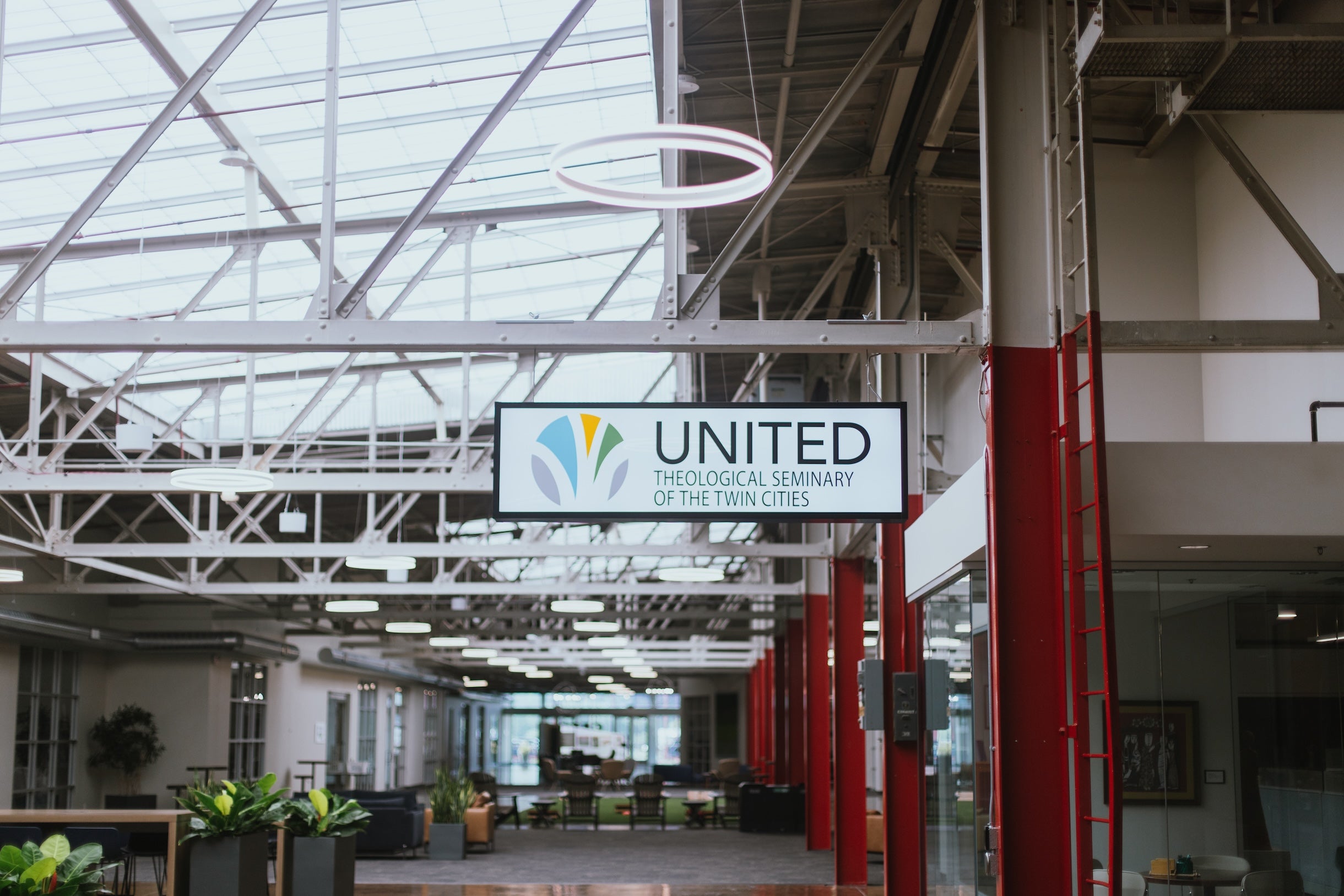 Image of a refurbished industrial building with plants and seating areas. A sign in the center reads "United Theological Seminary of the Twin Cities."